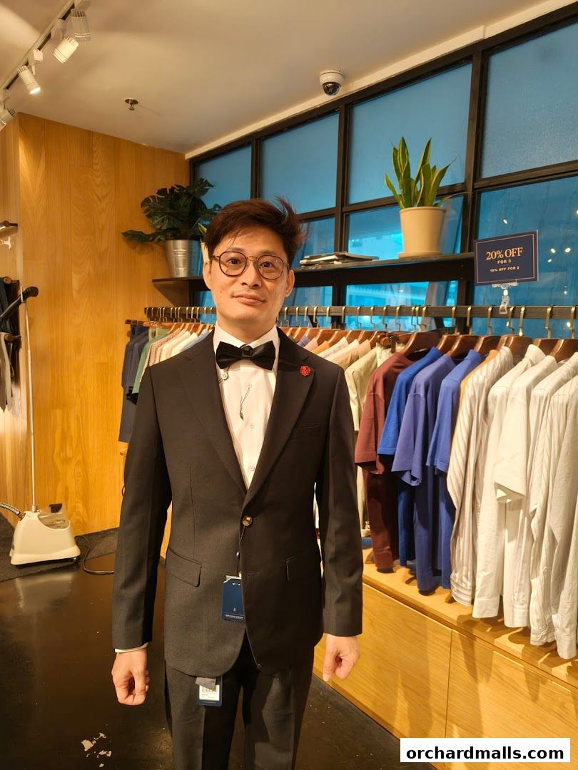 Man in a black suit with a bow tie stands in a clothing store.