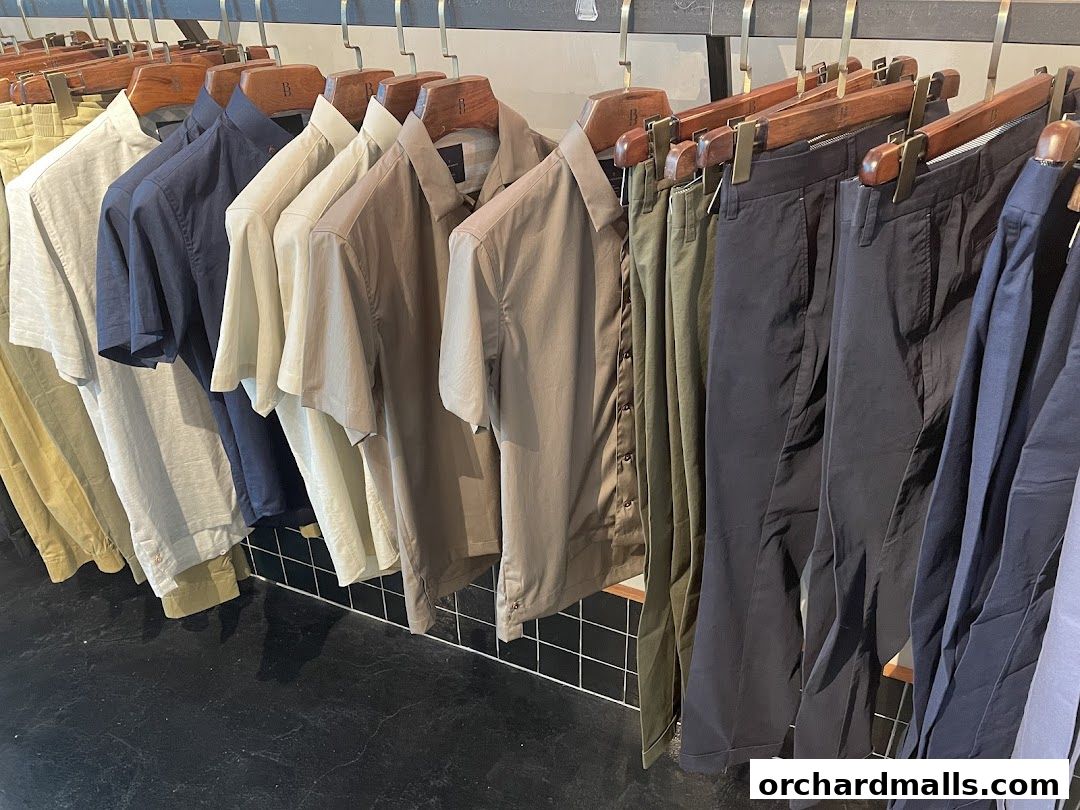 A rack of men's shirts and pants in neutral colors displayed in a store.