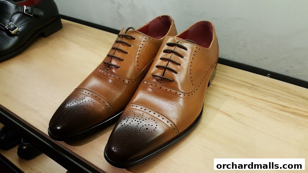 A pair of classic tan leather Oxford shoes with brogue detailing on a wooden shelf.
