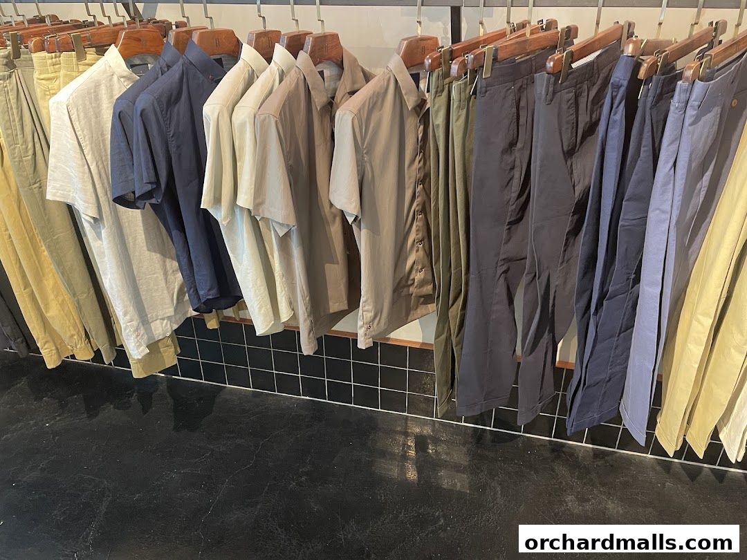 A rack of men's shirts and trousers in various neutral colors.
