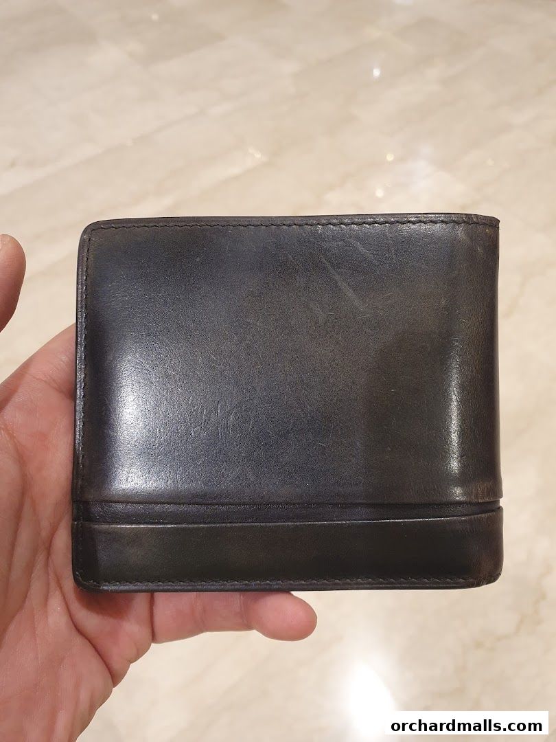 A hand holds a black leather wallet from Berluti.