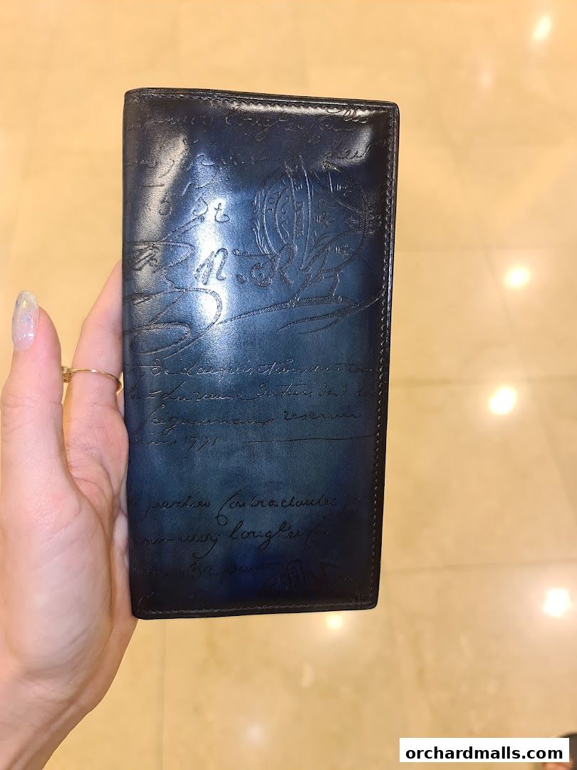 A hand holds a dark blue leather wallet with intricate script and embossed designs.