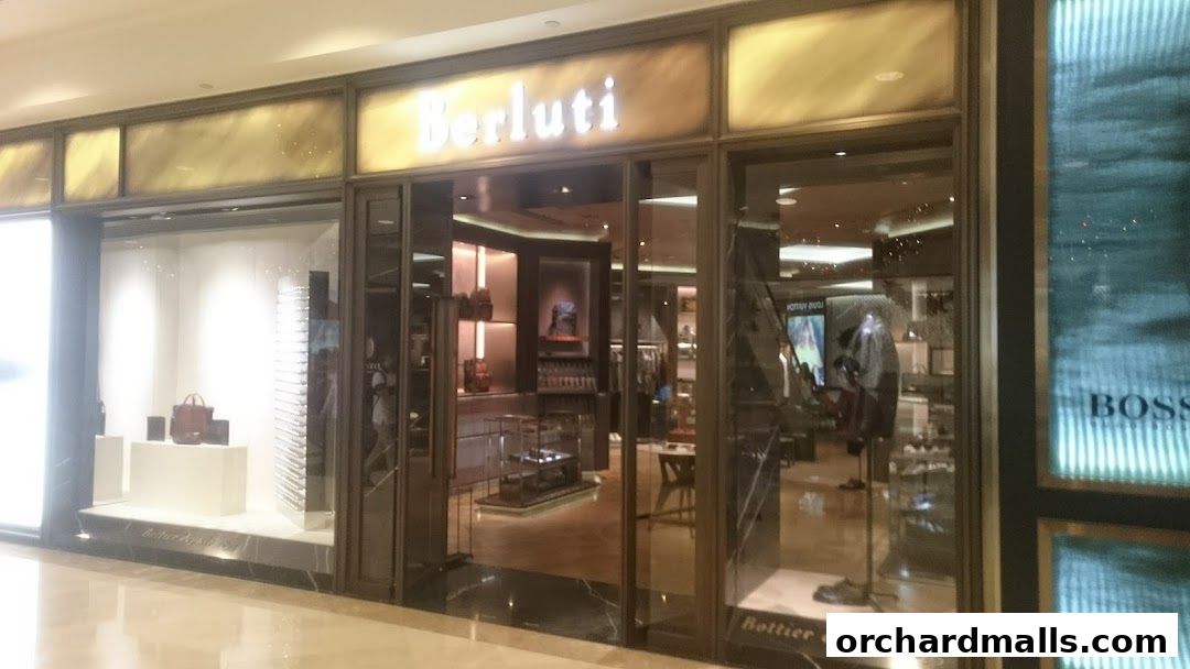 The exterior of a Berluti luxury fashion store with a well-lit interior showcasing bags and apparel.