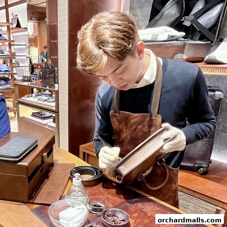 A craftsman meticulously works on a leather bag in a luxury retail store.