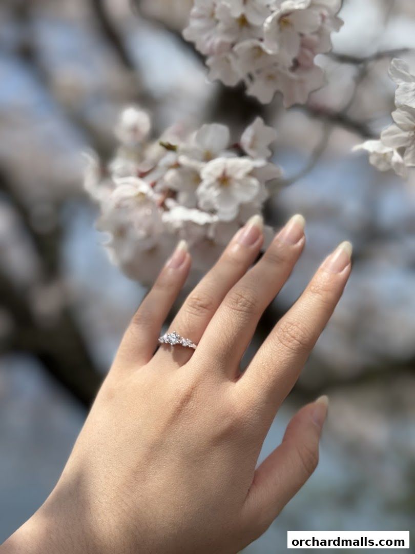 A hand with a delicate ring is shown against a backdrop of blooming cherry blossoms.