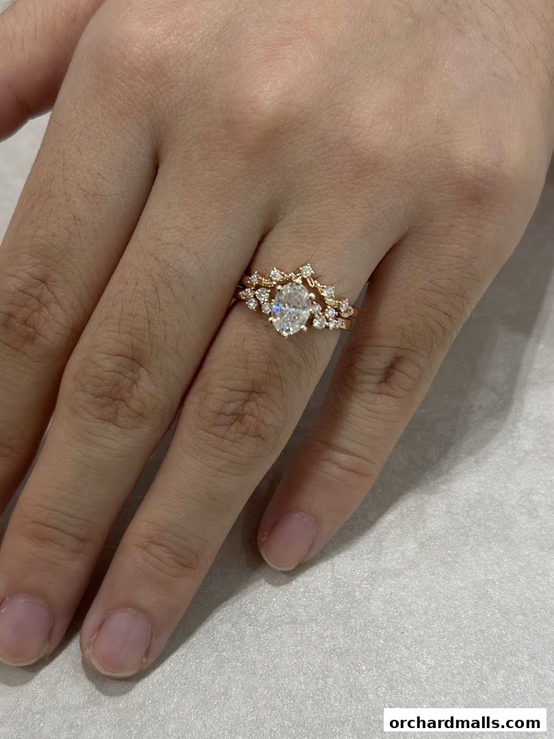A hand wearing a delicate oval diamond engagement ring with a matching wedding band.