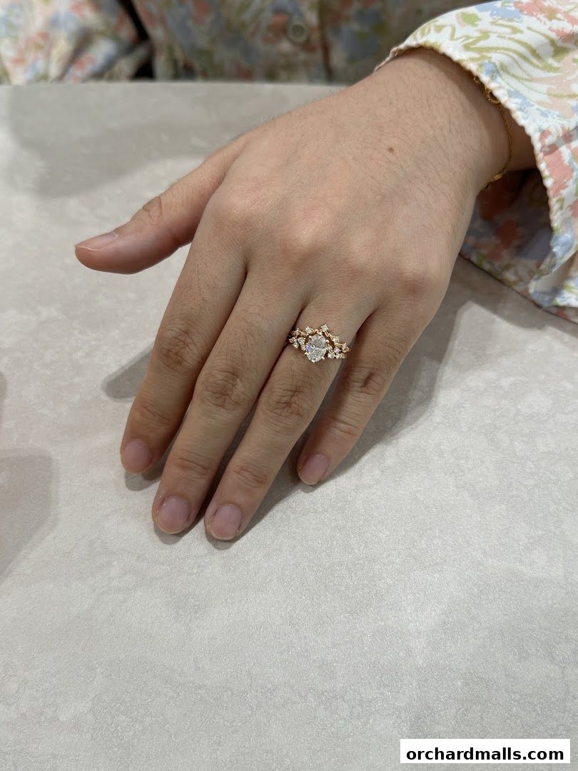 A hand wearing a delicate gold ring with a central oval stone and smaller accent stones.