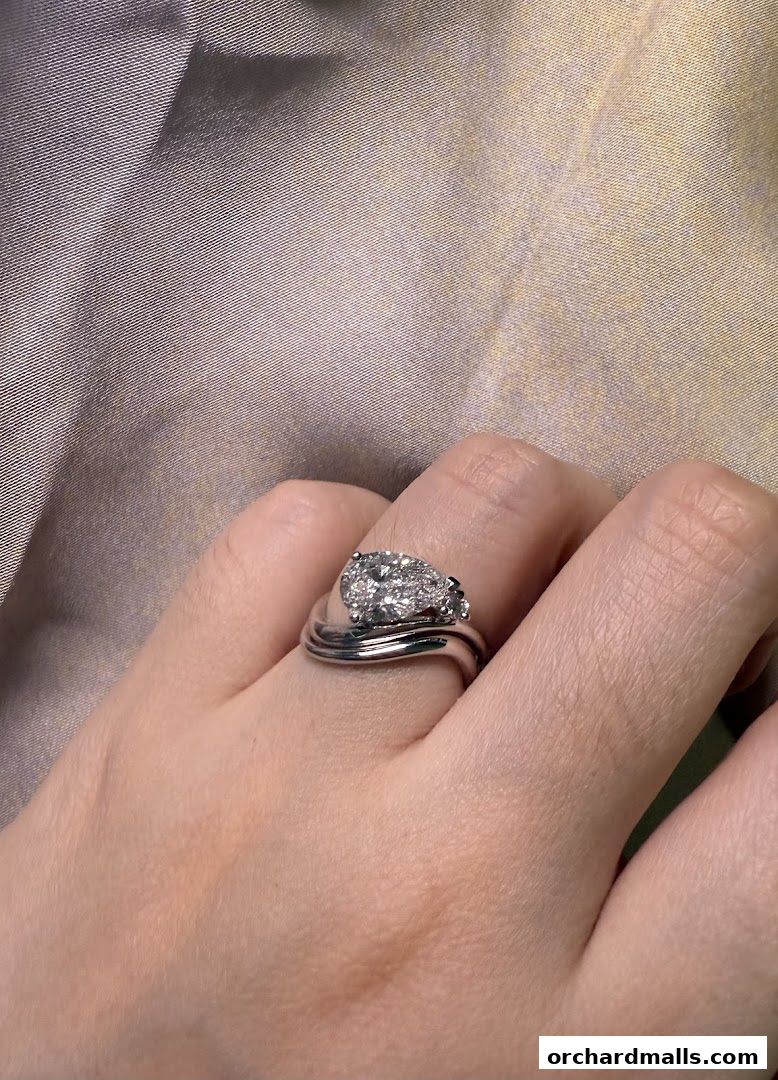 A hand wearing a pear-shaped diamond engagement ring and a wedding band.