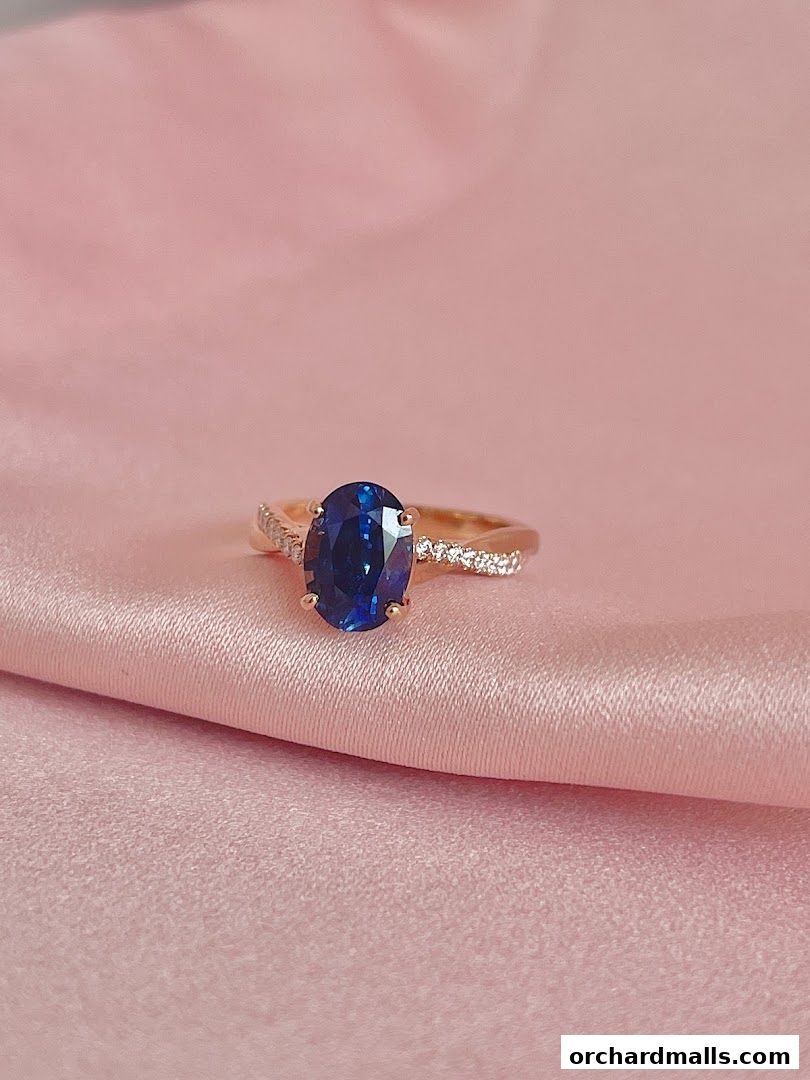 A stunning oval sapphire ring with diamond accents on a pink satin background.