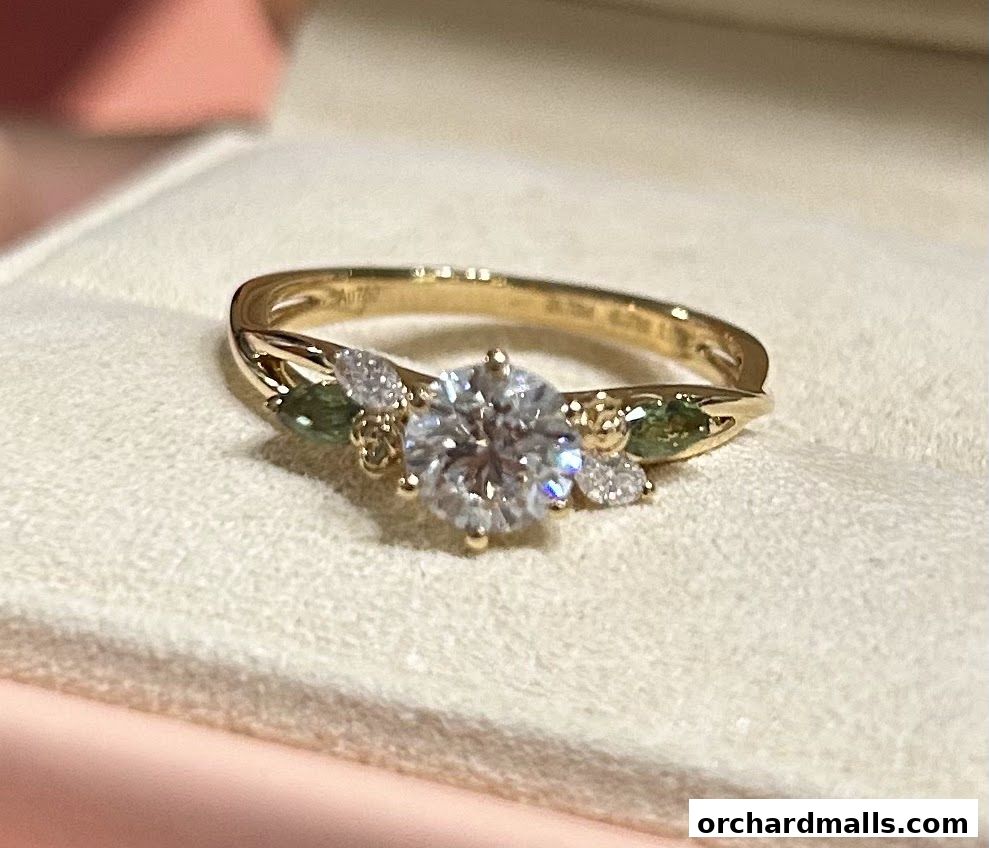 A close-up shot of a gold ring with a large diamond and green accent stones.