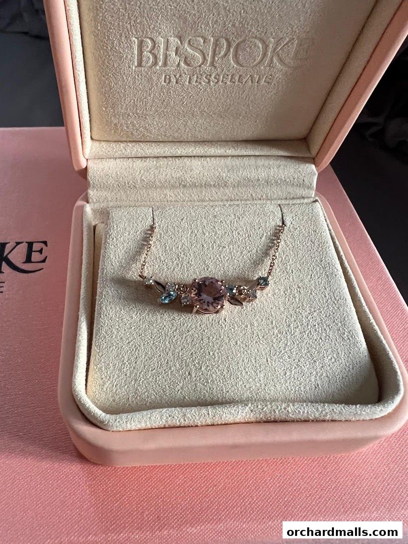 A delicate rose gold necklace with a central pink gemstone and smaller blue stones, presented in a pink velvet box.