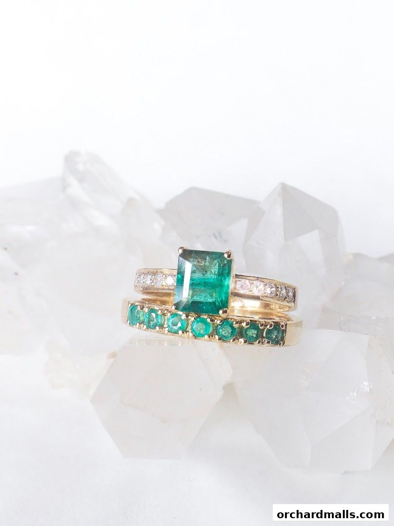Two gold rings with emeralds and diamonds displayed on clear crystals.
