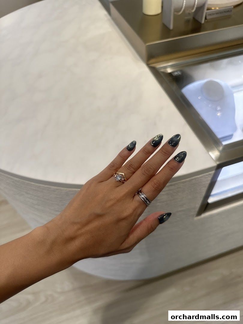A hand with rings and dark nail polish is shown in front of a jewelry display case.