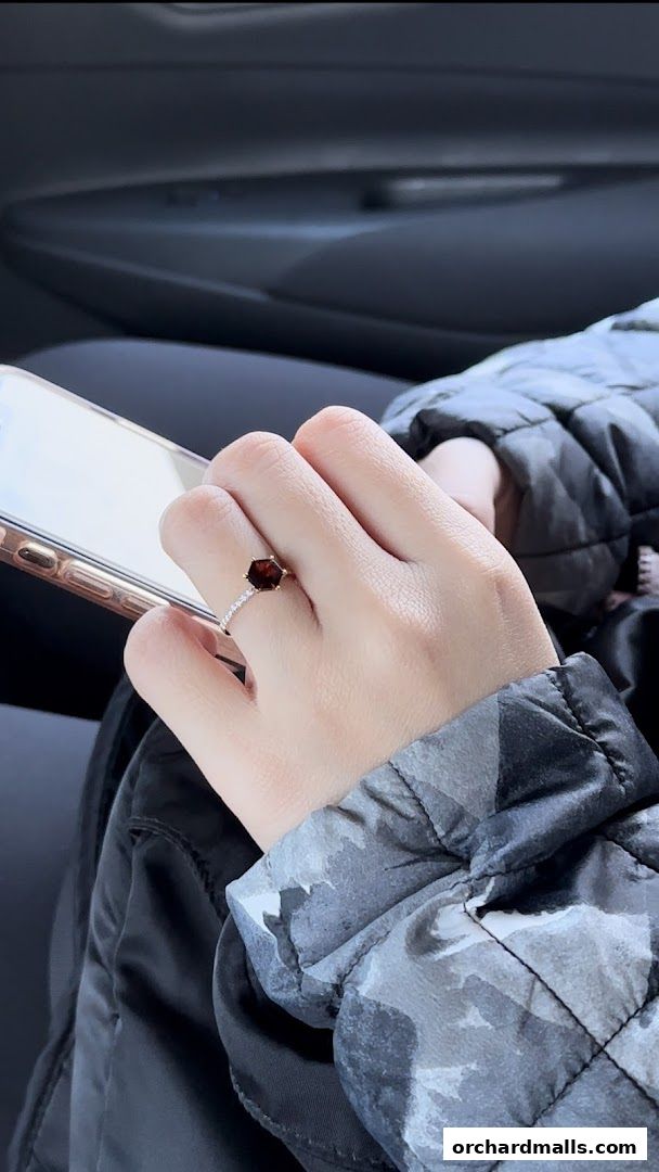 A hand wearing a hexagonal gemstone ring and holding a smartphone.