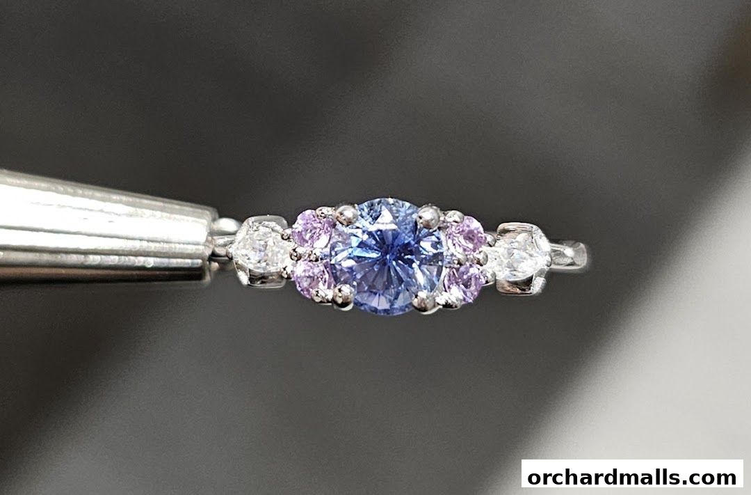 A close-up of a delicate ring with a blue center stone and pink and white accent stones.