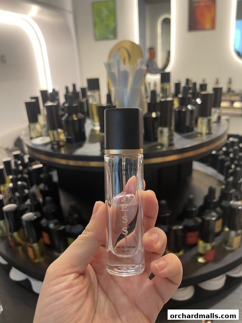 A hand holds a perfume bottle in front of a display of various fragrances.