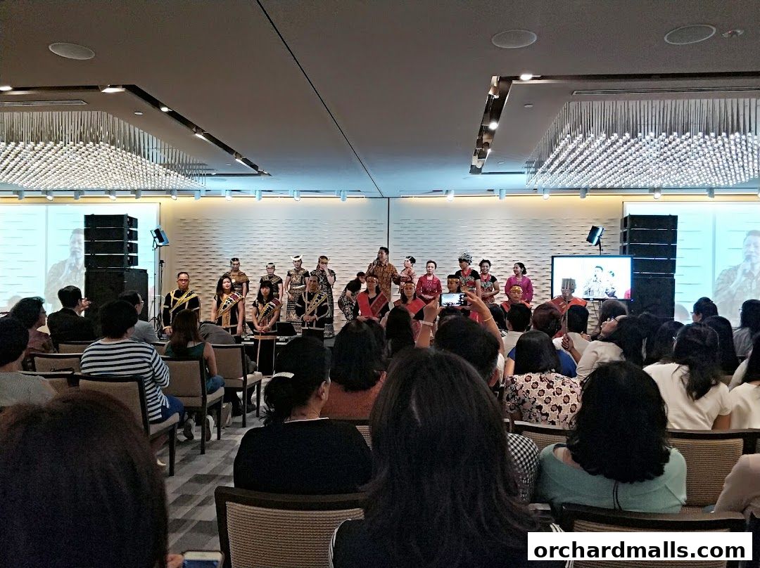 People in traditional attire perform on stage for an audience in a modern hall.