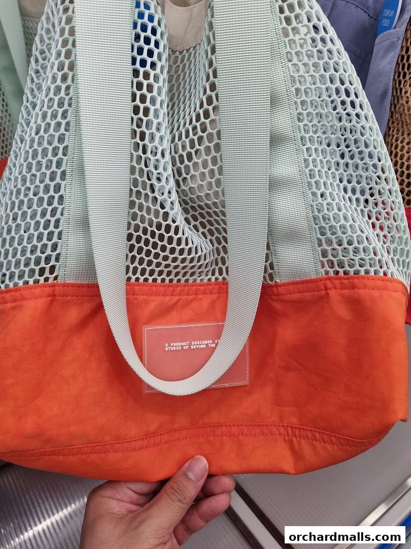 A close-up shot of a mesh tote bag with an orange base, held by a hand.