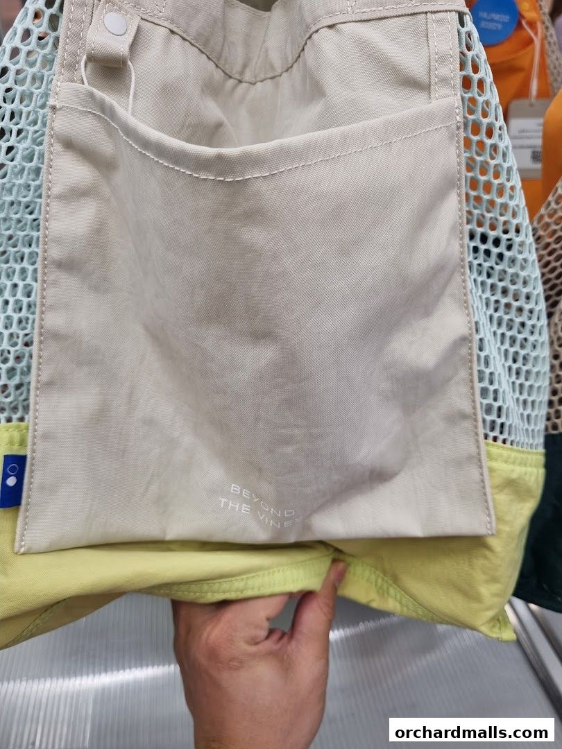 A close-up of a beige tote bag with a mesh side pocket and a hand holding it.
