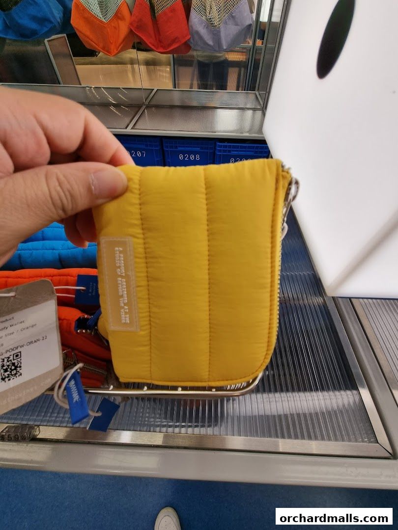 A hand holds a yellow quilted wallet in front of a display of bags.