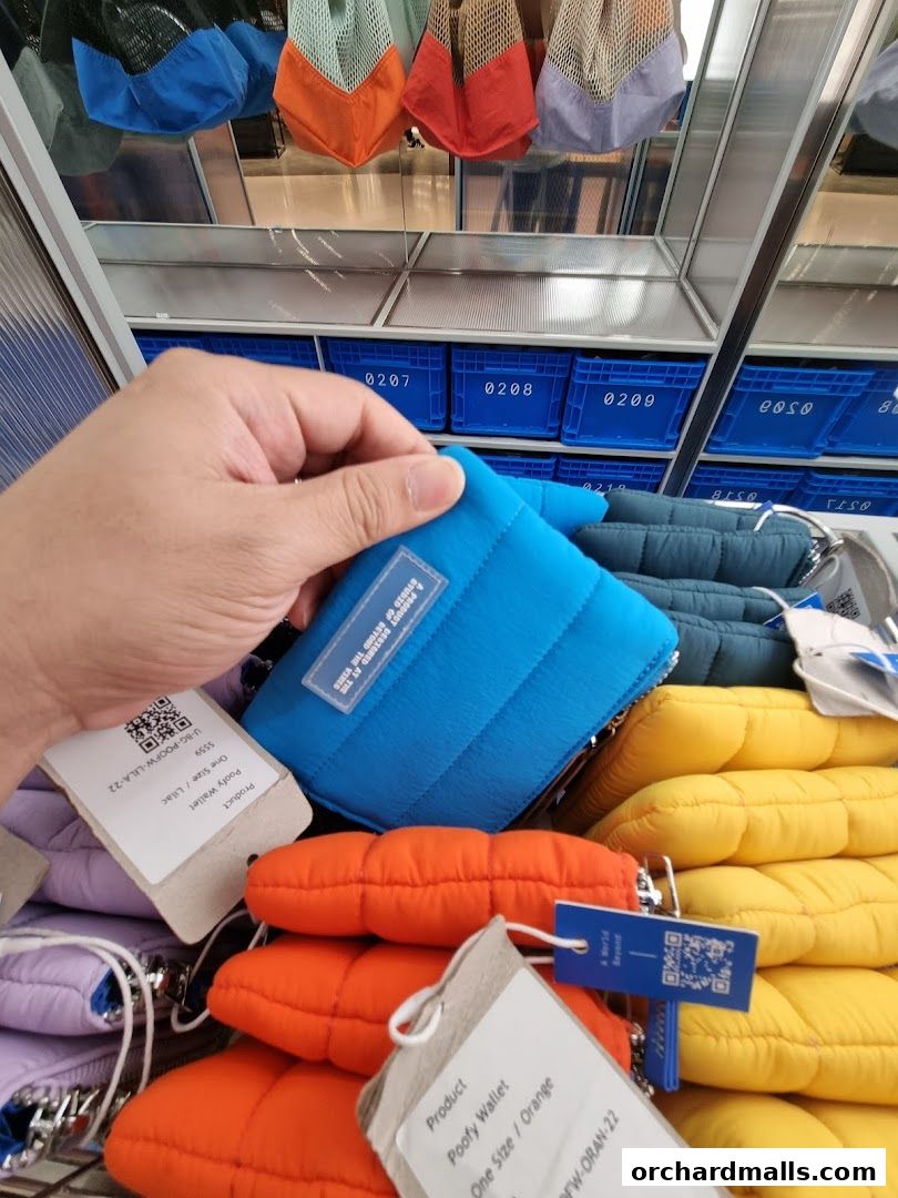 A hand holds a blue quilted wallet, with stacks of orange and yellow wallets behind it.
