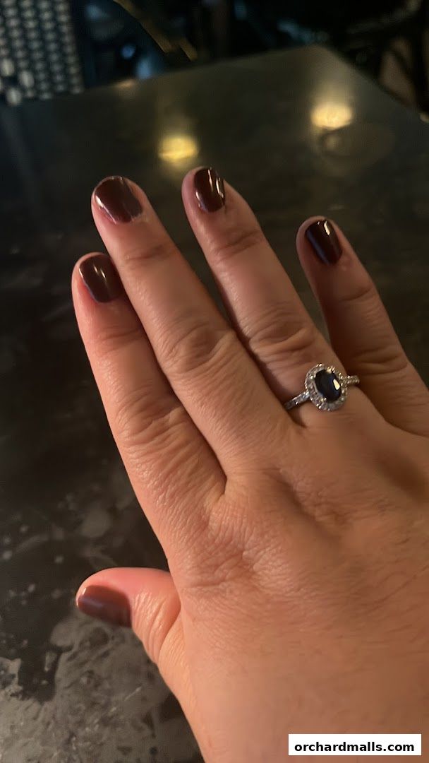 A hand with dark red nail polish and a diamond ring is shown.