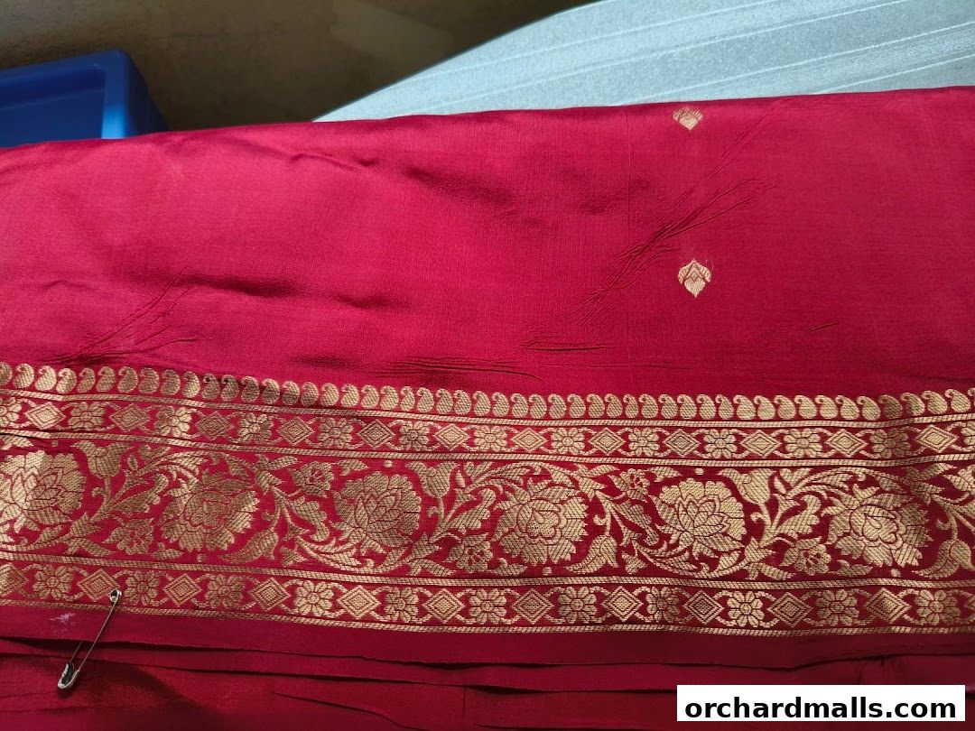 A close-up of a vibrant red fabric with intricate gold floral embroidery and a safety pin.