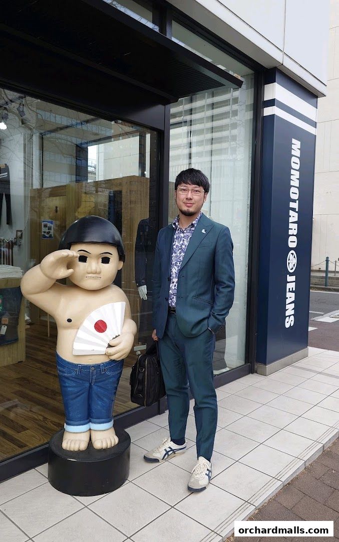 A man in a suit stands next to a statue outside a store called Momotaro Jeans.