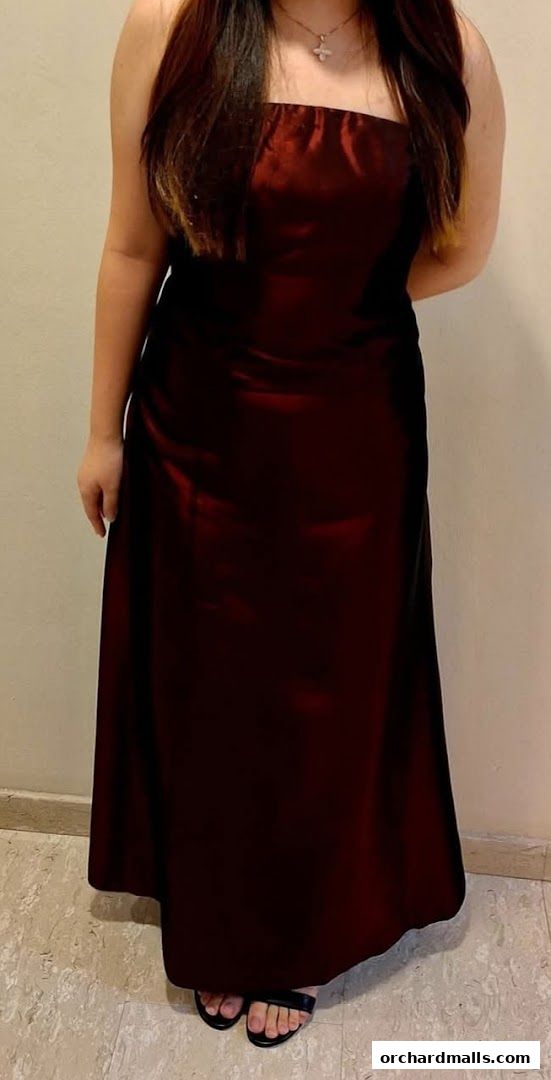 A person wearing a strapless, floor-length, dark red satin dress and black sandals.
