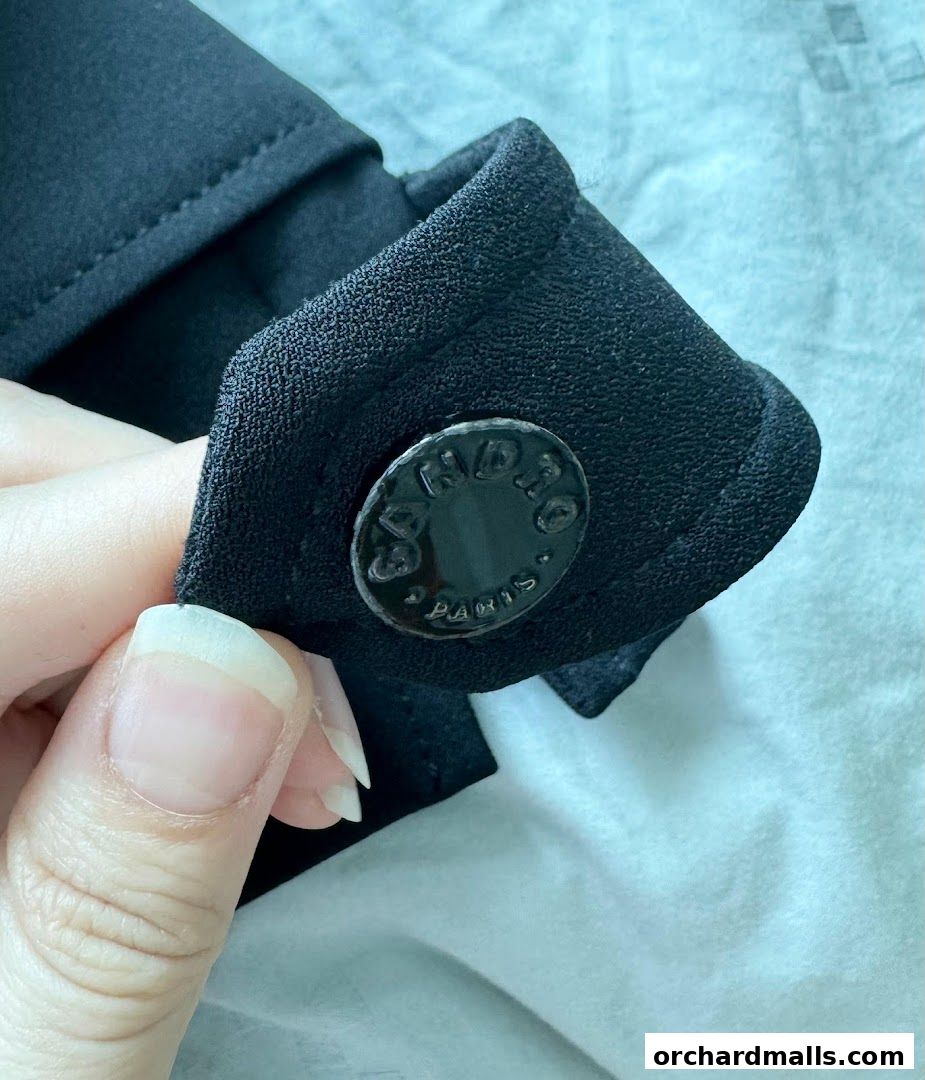 Close-up of a black fabric cuff with a shiny button and a hand holding it.