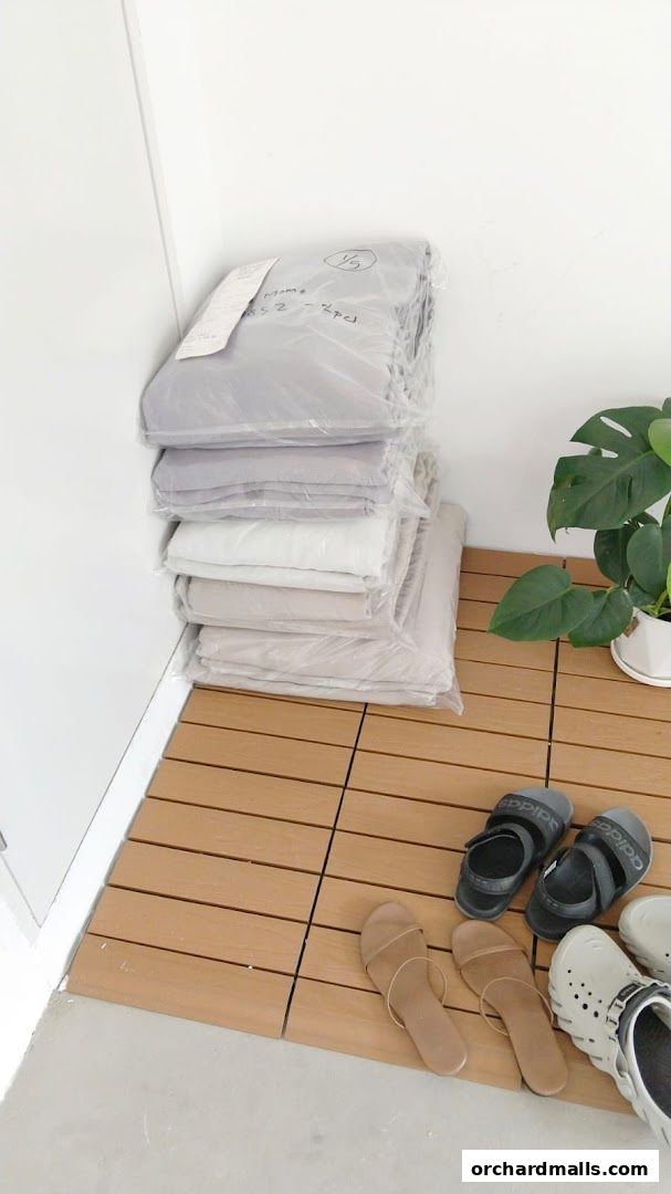 Stack of neatly folded clothes in plastic bags, with sandals and a plant nearby.