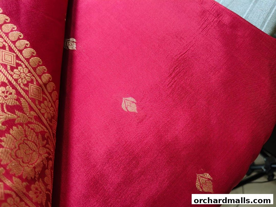 Close-up of a vibrant red fabric with intricate gold embroidery and subtle leaf patterns.