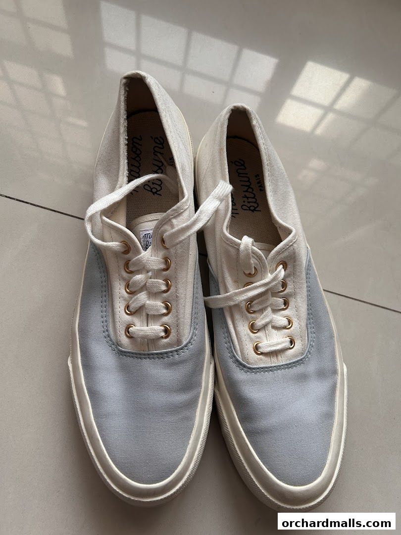 A pair of light blue and white canvas sneakers with white laces and gold eyelets.