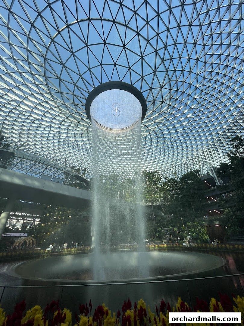 Indoor waterfall with lush greenery and a geodesic dome ceiling.
