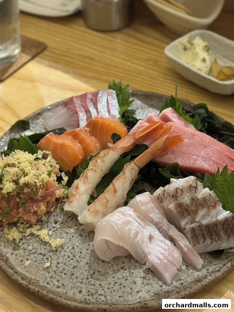 A plate of assorted sashimi, including salmon, tuna, shrimp, and white fish, garnished with greens.