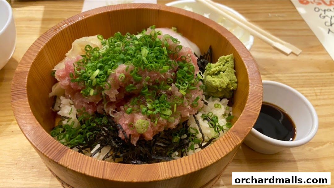 A wooden bowl filled with rice, raw tuna, green onions, and wasabi.