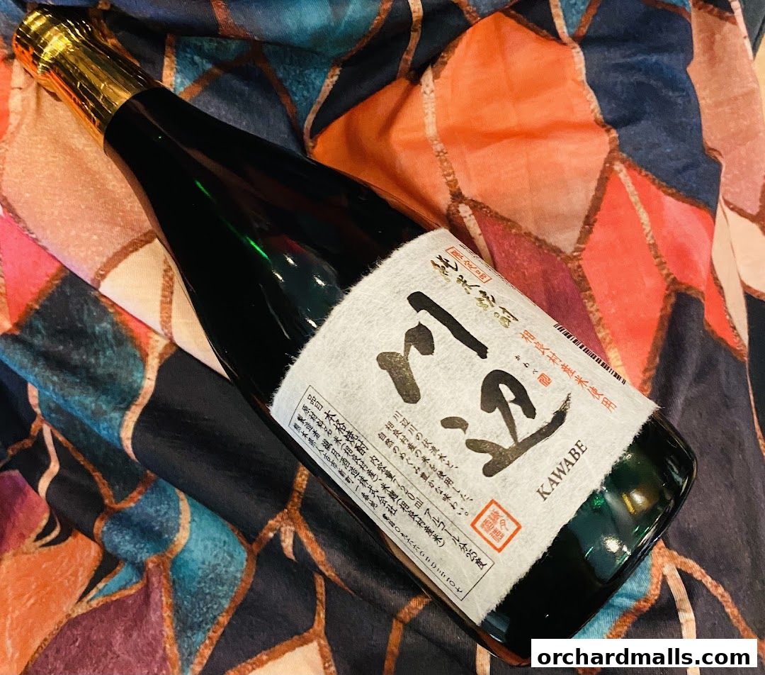 A bottle of KAWABE sake rests on a colorful, abstract patterned fabric.