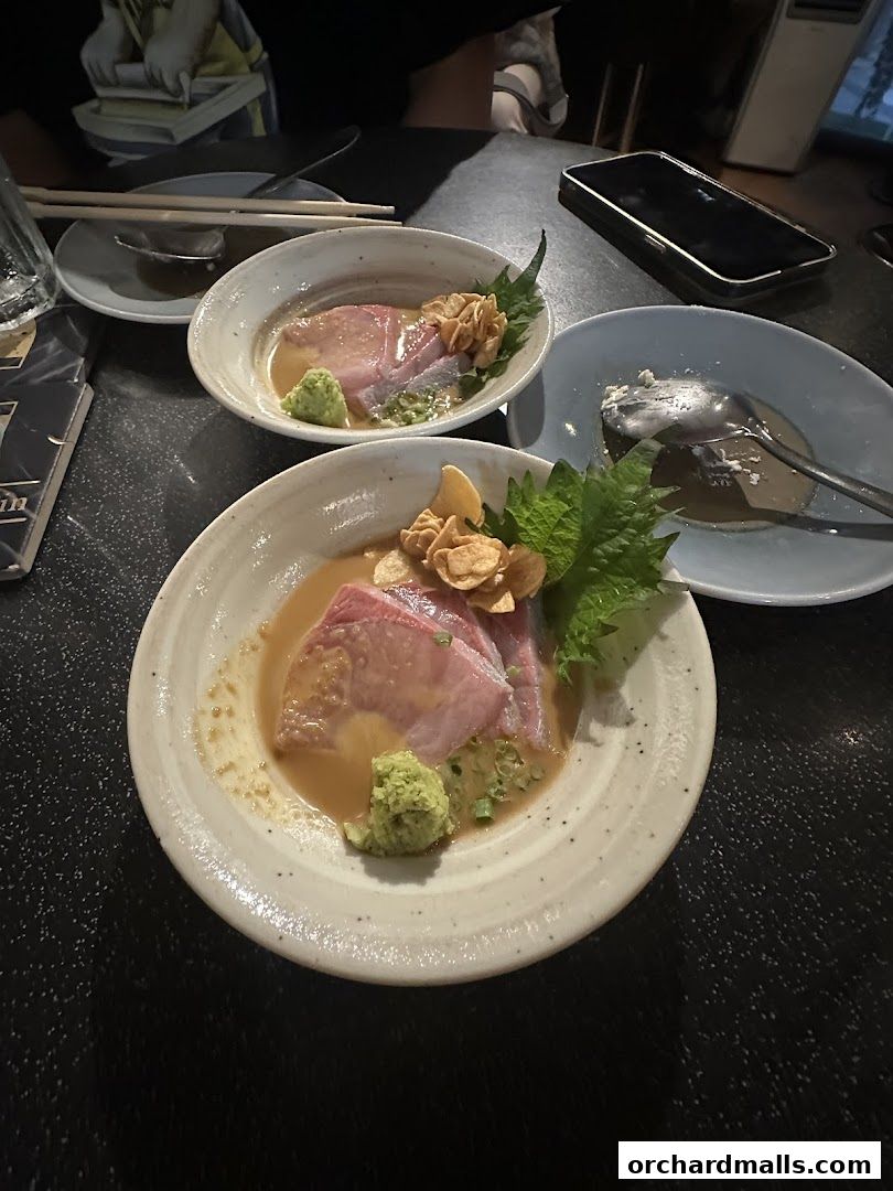 Two plates of sashimi with wasabi and garnishes on a dark table.