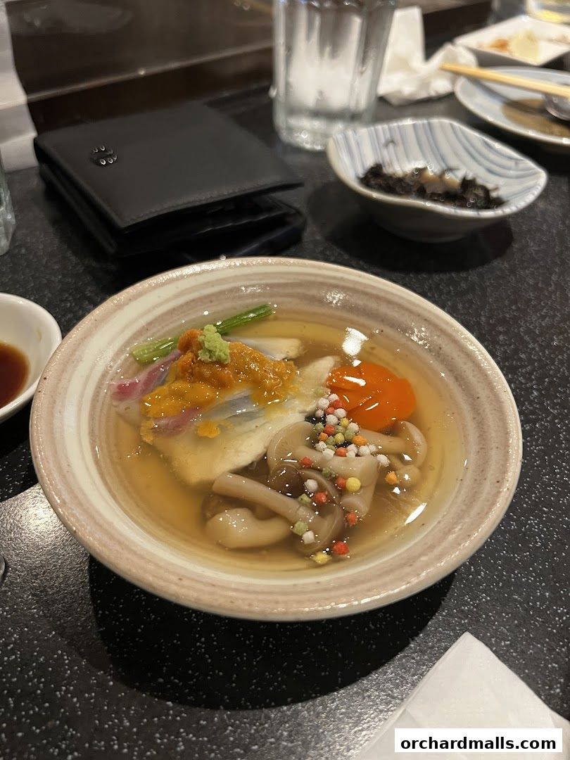 A close-up of a delicate Japanese dish with seafood, vegetables, and mushrooms in broth.