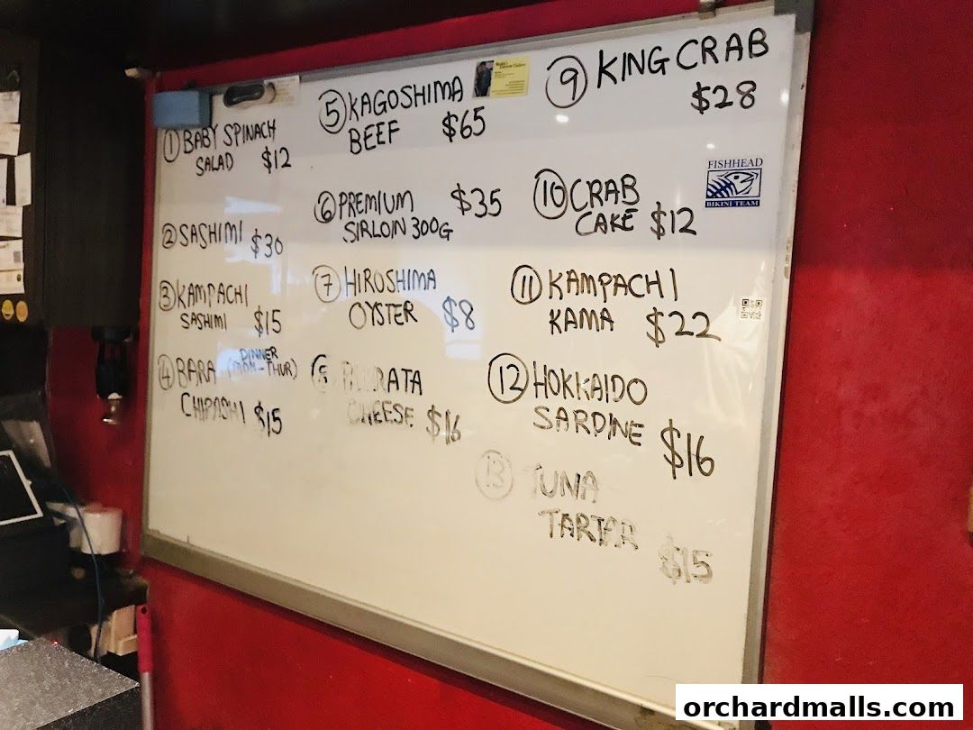 A whiteboard menu with Japanese food items and prices, including sashimi and seafood.