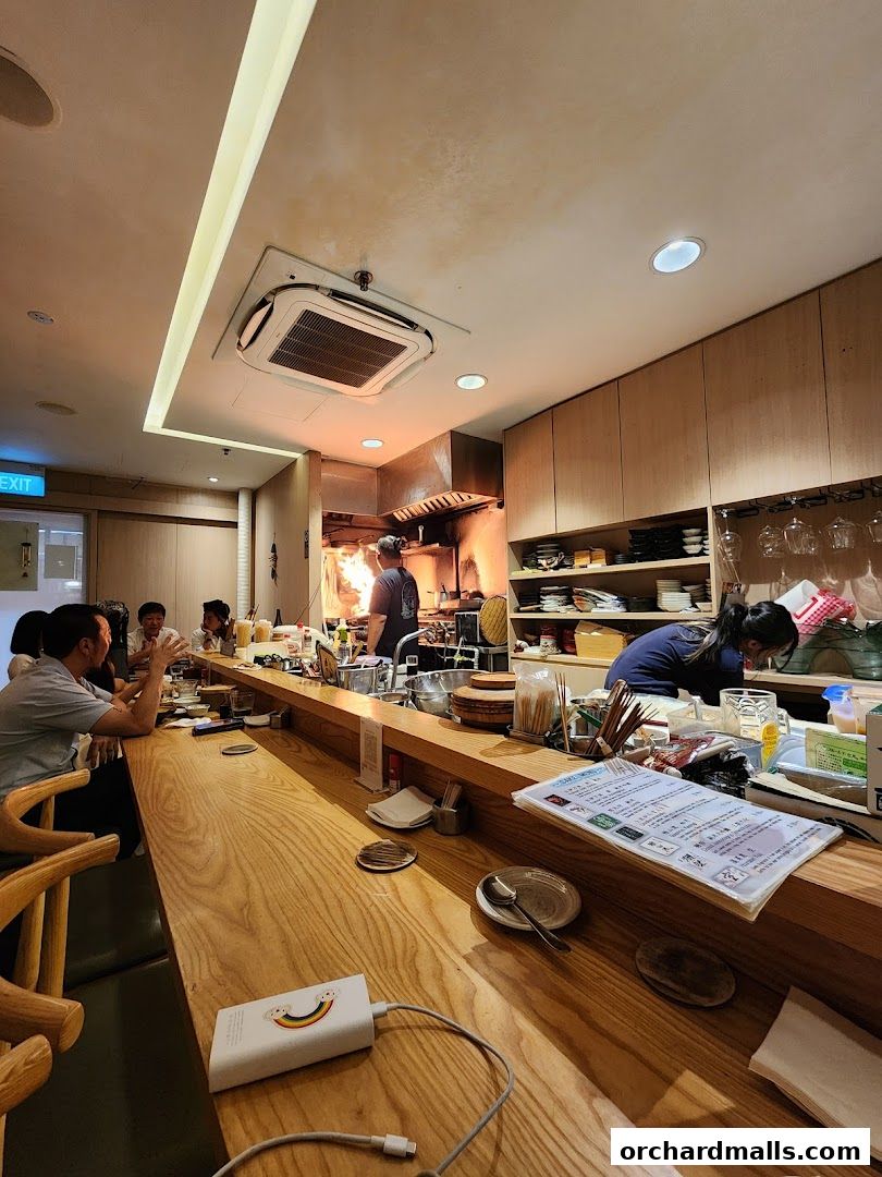 Diners seated at a wooden counter in a restaurant with an open kitchen.