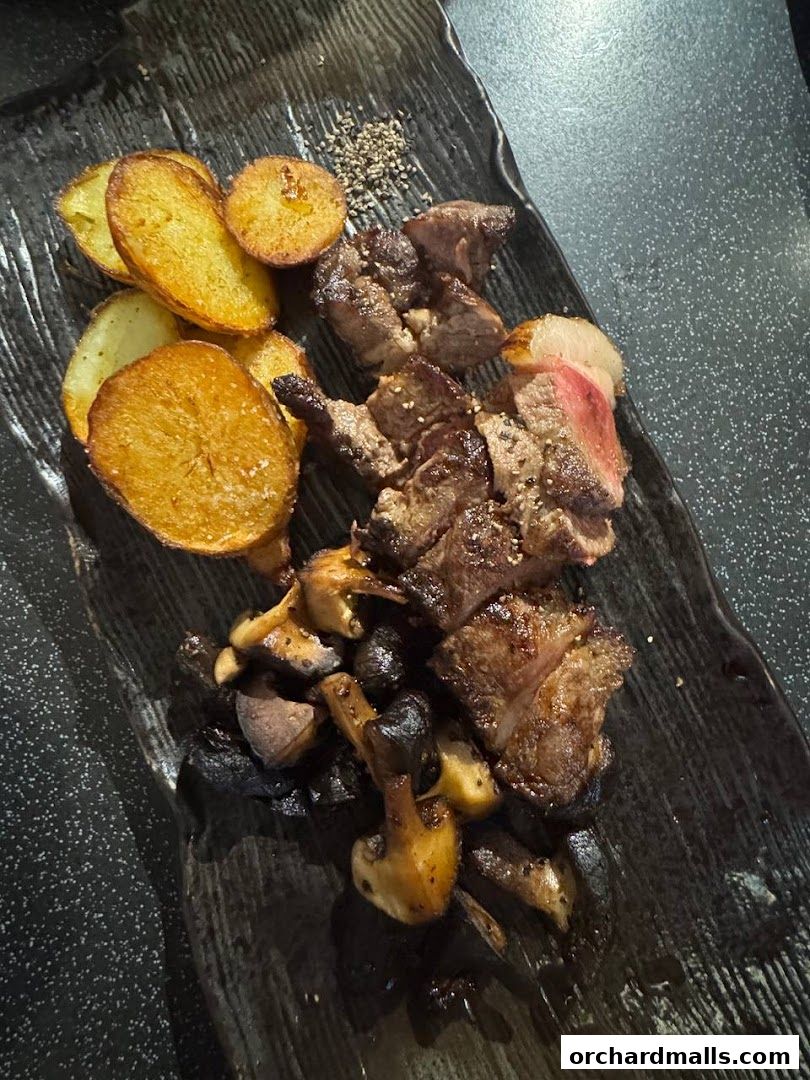 A plate of sliced steak, roasted potatoes, and mushrooms seasoned with pepper.