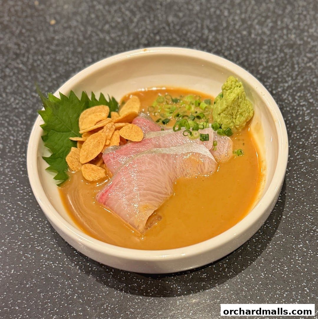 A bowl of thinly sliced raw fish with sauce, crispy garlic, and wasabi.