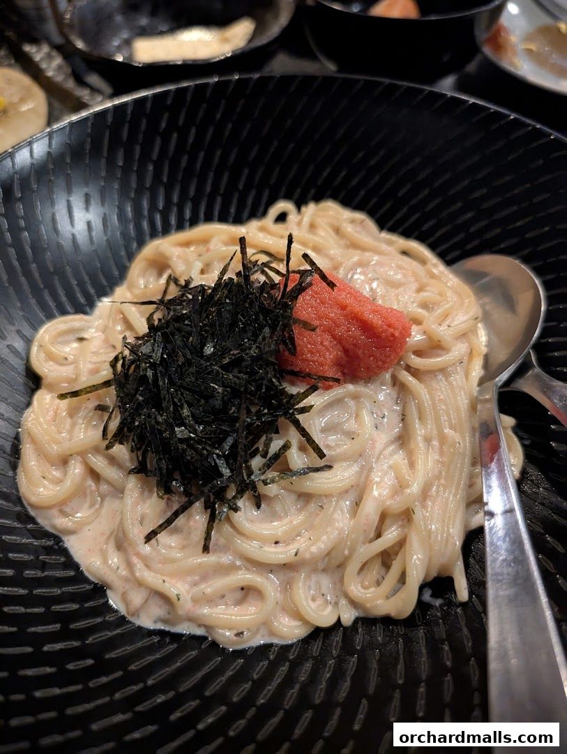 A close-up of a creamy pasta dish topped with seaweed and roe in a black bowl.