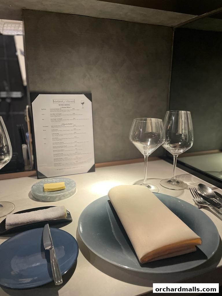 A table setting with a wine menu, glasses, plates, and cutlery at Bistro Etroit.