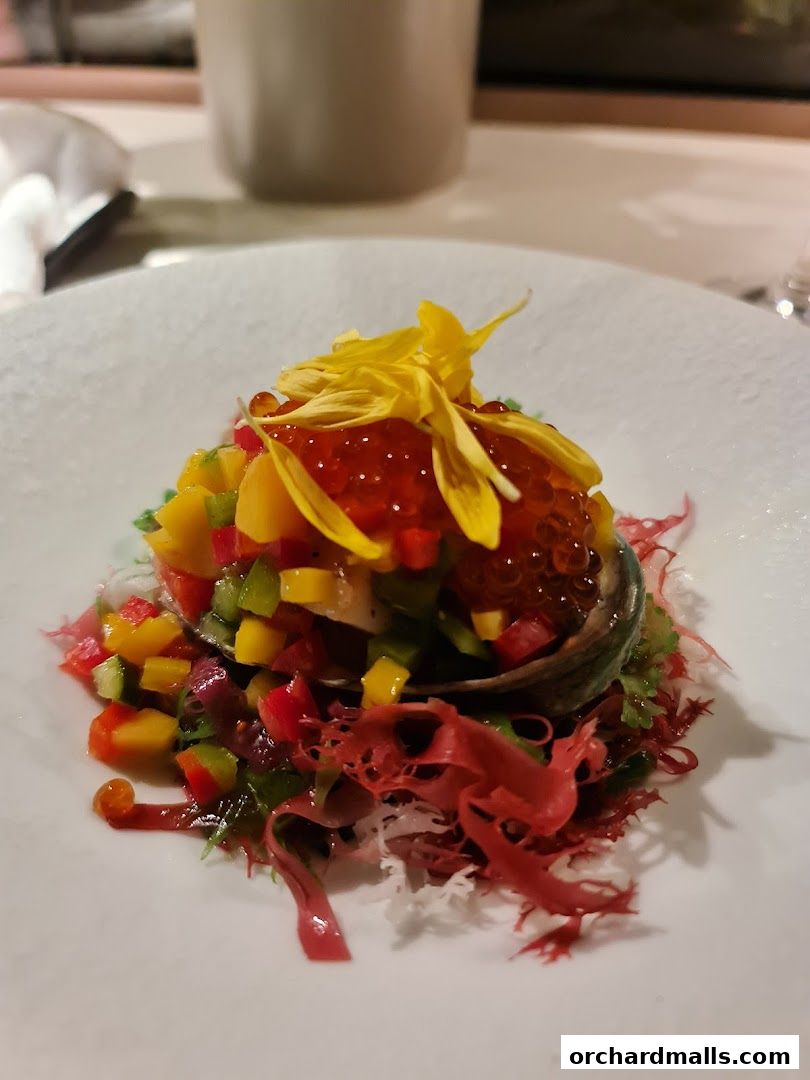 A beautifully plated dish with abalone, roe, diced vegetables, and edible flowers.