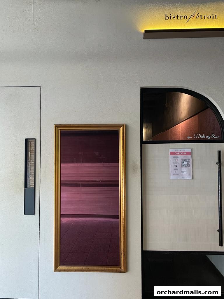 The entrance of Bistro Etroit Ep.2 with a golden framed mirror and a sliding door.