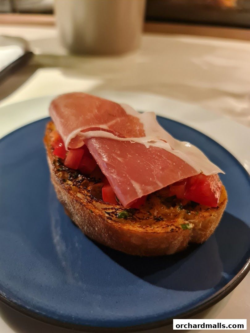 A close-up of a bruschetta topped with prosciutto and diced tomatoes on a blue plate.