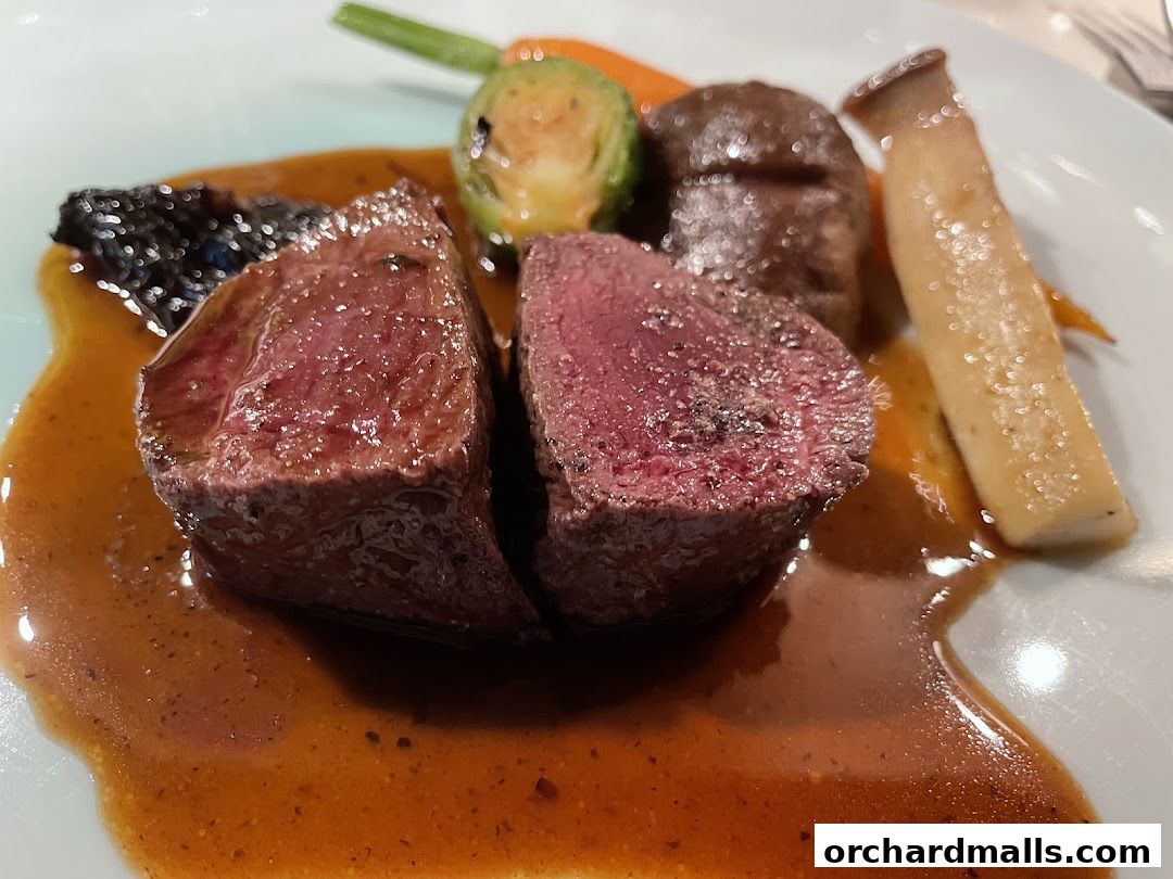 A close-up of a perfectly cooked steak with vegetables and sauce on a white plate.