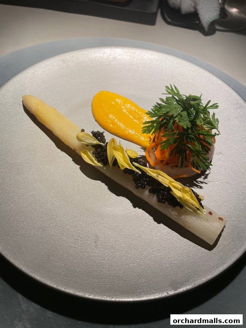 A gourmet dish featuring white asparagus, caviar, and a vibrant orange sauce.